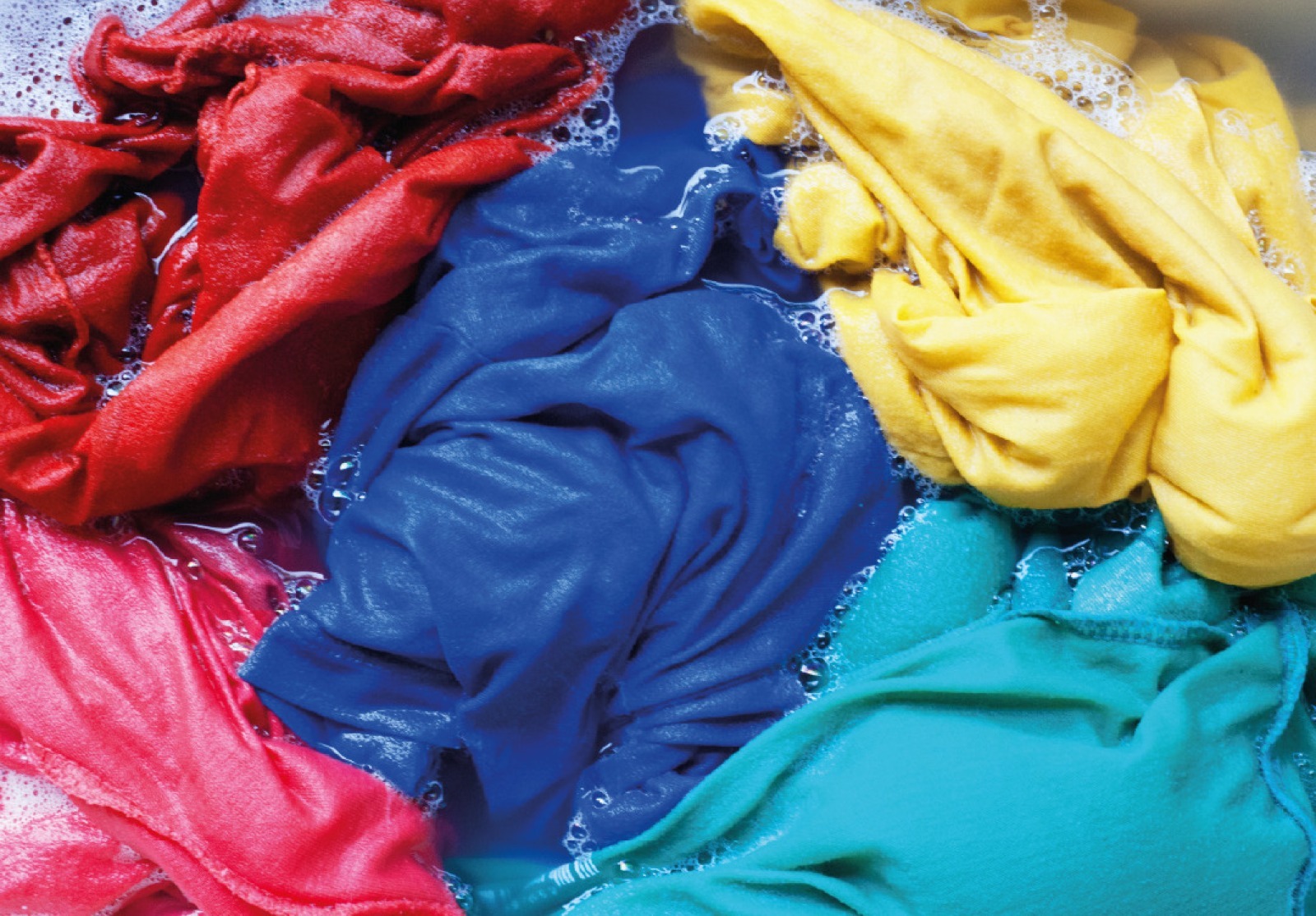 Visão interna do tambor de inox de uma máquina de lavar roupas, com peças coloridas em tons de azul, amarelo e vermelho..